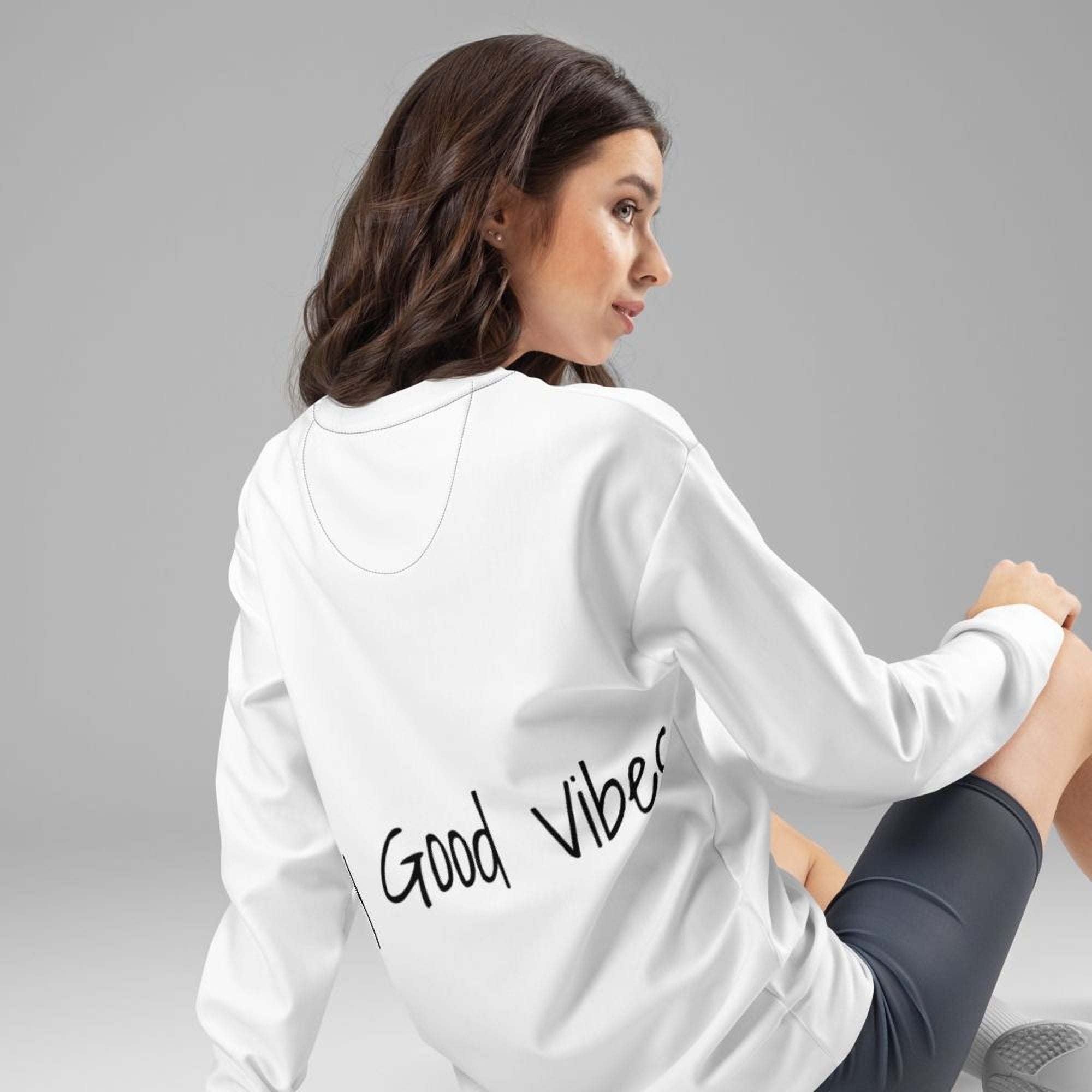 A woman with long brown hair is sitting on the floor wearing a white sweatshirt with the text "Good Vibes" printed on the back.