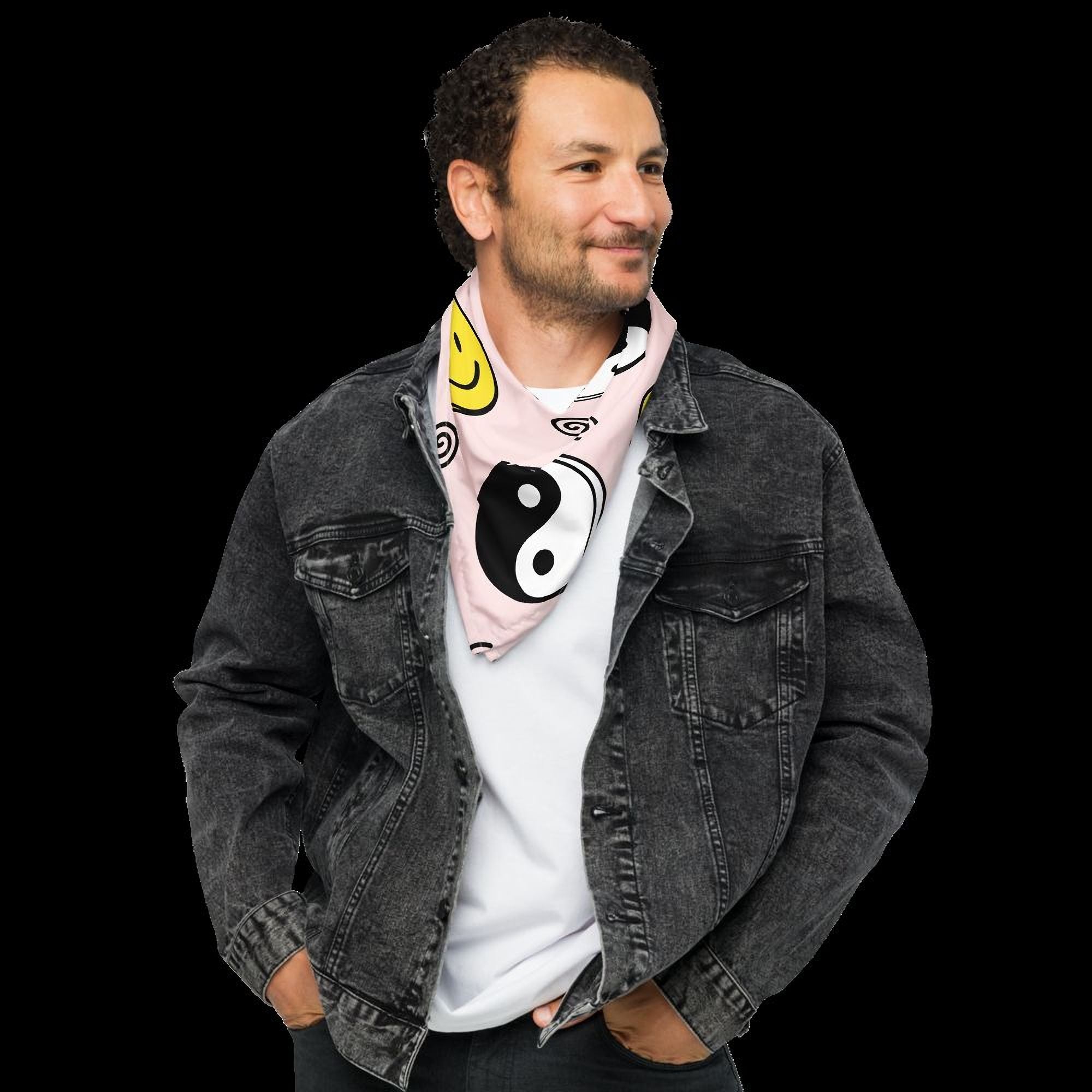 A man wearing a gray denim jacket and a pink and white scarf with a yin and yang design stands against a black background.